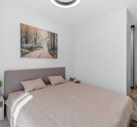 Bedroom in a 2-room apartment with a bed, a painting, and a plant, floor with wooden decor.