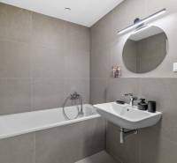 Bathroom in a 2-room apartment with a shower, sink, and round mirror.