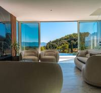 Interior of a villa with large windows, view of greenery and pool.