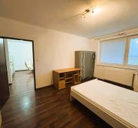 A bedroom in a two-room apartment with a wooden decor floor and simple furniture.