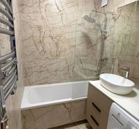 Bathroom with a bathtub, sink, and washing machine in a 2-room apartment. Tiles with a marble appearance.