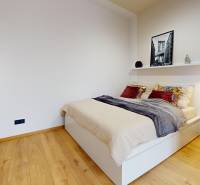 A bedroom in a studio apartment with a bed, shelf, table, and floor with a wooden decor.