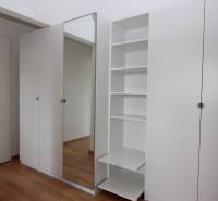 White built-in wardrobe with mirror and shelves in a studio apartment.