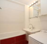 A bathroom with a bathtub, sink, and washing machine in a studio apartment. White and red tiles.
