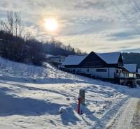 A snowy street in Mýto pod Ďumbierom with a view of houses and the surrounding landscape.