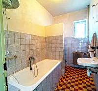 A bathroom in a family house with a bathtub, a sink, a radiator, and checkered tile flooring.