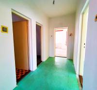 A corridor in a family house with a green floor, white walls, and several doors.