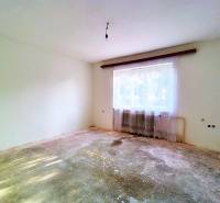 An empty room in a family house with a worn-out floor, a radiator, and curtains.