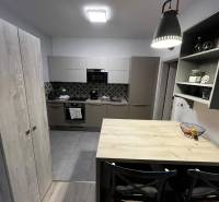 A kitchen in a 2-room apartment with tiles, a wooden decor floor, and dark gray cabinets.