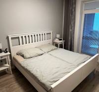 A bedroom with a wood-decor floor and a simple bed in a two-room apartment.