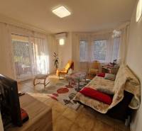 Living room of a family house with a television, sofa, coffee table, and large windows with curtains.