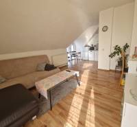 Attic living room in a family house with a sofa, dining table, and wooden decor flooring.