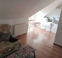 Attic space in a family house with a kitchen, a floral sofa, and a wooden decor floor.