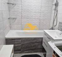 A bathroom in a 3-room apartment with a bathtub, shower, and washing machine on white tiles.