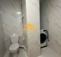 Bathroom in a 2-room apartment with a washing machine and toilet, tiled with a white tile design.