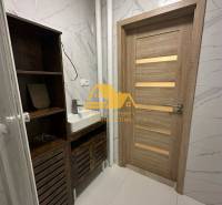 Bathroom in a 2-room apartment with a sink, cabinet, wooden door, and white tiles.