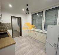 A kitchen in a studio apartment with a wood-patterned floor and white appliances.