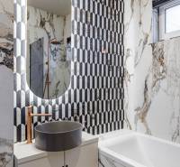 A bathroom with marble tiles, an oval mirror, and a freestanding sink in a 2-room apartment.