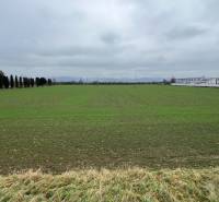 Lands - commercial in Pruské with greenery, tree lines, and industrial buildings in the background.