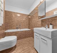 Bathroom with a bathtub and a wall-hung toilet in a 2-room apartment with light tiles.