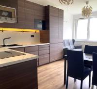 A kitchen in a 3-room apartment with dark furniture and a wooden decor floor.