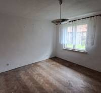 An empty room with a window, chandelier, and wooden-patterned floor in a family house.