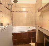 A bathroom in a 2-room apartment with a corner bathtub and beige tiles.