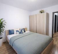 A bedroom in a 2-room apartment with a bed, wardrobe, and wooden decor flooring.