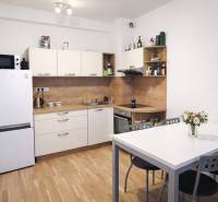 A kitchen in a 2-room apartment with a refrigerator, table, and wooden decor flooring.