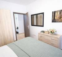 Bedroom in a two-room apartment with a wardrobe, dresser, and wooden decor flooring.