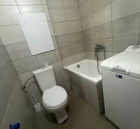 Bathroom of a one-room apartment with a washing machine, bathtub, and toilet.