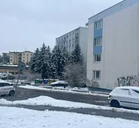 A snowy Bazovského street in Zvolen with parked cars next to a multi-story building.