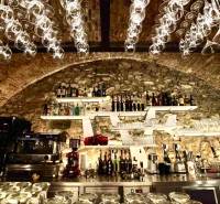 A bar with a vaulted ceiling, hanging glasses, stone decor, and alcohol in a gastro space.