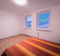 A bright room with two windows, a bed, and a floor with a wooden decor.