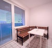 Dining nook with white tiles, a window, and a corner bench in a two-room apartment.