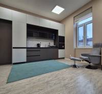 A kitchenette with white cabinets and a carpet in a studio apartment, wooden decor flooring.