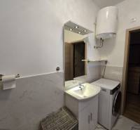 Bathroom of a holiday apartment with a washing machine, sink, and gas water heater.