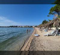 A sandy beach by the sea with loungers under straw umbrellas, clear sky, and calm water.