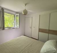 Bright bedroom with a window, white wall, and wardrobe in a family house.