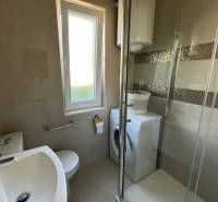 A bathroom in a family house with a shower, a washing machine, and a window.