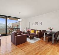 Living room of a two-room apartment with a seating area, dining table, and wooden decor flooring.