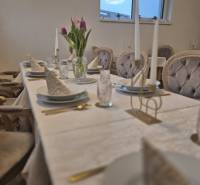 A table with a white tablecloth, plates, glasses, flowers, and chair covers in a dining area.
