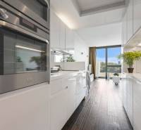 A kitchen in a 2-room apartment with glossy white cabinets and a floor with a wood decor.
