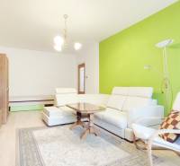 Living room in a two-room apartment with white furniture, a green wall, and a floor with a wooden decor.