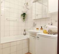 Bathroom in a 2-room apartment with a shower, sink, and washing machine, bright tiles.