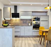 A kitchen in a studio apartment with a wood-patterned floor, a dining table, and yellow chairs.