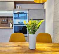 A kitchen in a studio apartment with a wooden decor, a flower vase on the table, yellow chairs.
