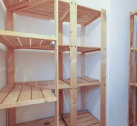 Wooden shelves in the pantry of a two-room apartment with white walls.