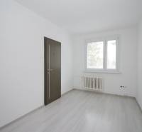 A room in a 3-room apartment with white walls, a wooden decor floor, and a window.