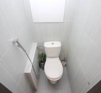 A toilet in a 3-room apartment with beige tiles and a detail of a shower head.